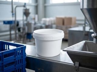 White 560 ml plastic bucket with lid on a dairy plant conveyor belt next to a stack of plastic crates