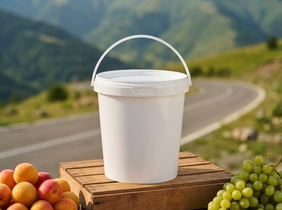 White 900 ml plastic bucket with lid and molded-in handle on a wooden crate at a roadside fruit stand, next to a pile of apricots