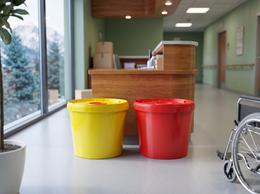 Yellow and red 11.5 liter medical waste buckets by a nurses' station in a hospital ward corridor