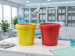 Yellow and red 1-liter medical waste buckets on a cabinet next to a dental chair
