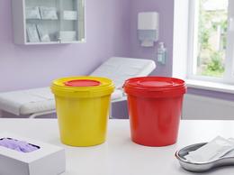 Yellow and red 1-liter medical waste buckets on a table in a private clinic treatment room