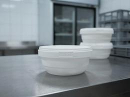 White shallow 385 ml plastic container with lid on a prep table in a ready-meal kitchen