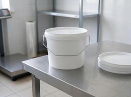 White 2.3 liter plastic bucket with a metal bail handle and lid on a packing line table