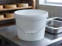 White 8 liter plastic bucket with lid and steel bail handle on a table in a cheese dairy