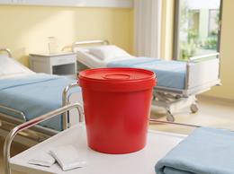 Red 5.6 liter medical waste bucket on a treatment cart in a hospital ward