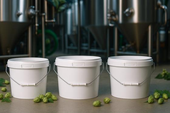 Three white buckets of hops against brewery tanks