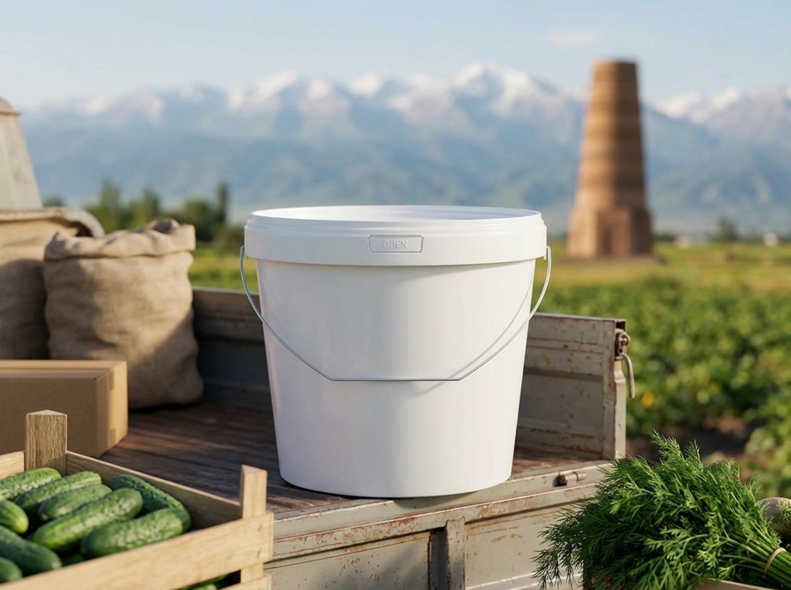 托克马克郊外的菜地旁，一只 5.6 升白色带盖塑料桶放在货车车厢挡板上，配金属提手，远处是布拉纳塔（Burana）