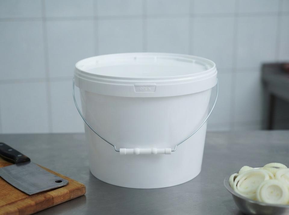 White 8 L plastic bucket with a metal bail handle, plastic grip, and lid on a steel table in a Rudny meat plant, next to a cleaver on a cutting board