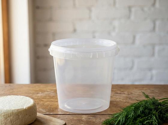 Clear 1 L plastic bucket with lid on a wooden counter at a farm shop in Tokmok next to a wheel of homemade cheese