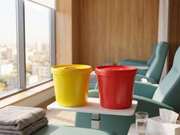Yellow and red 5.6 liter medical waste buckets on a table in a day hospital treatment room